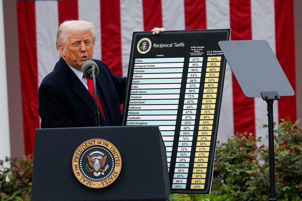 With a giant flag behind him, President Donald Trump stands beside a chart listing global tariffs in the Rose Garden.